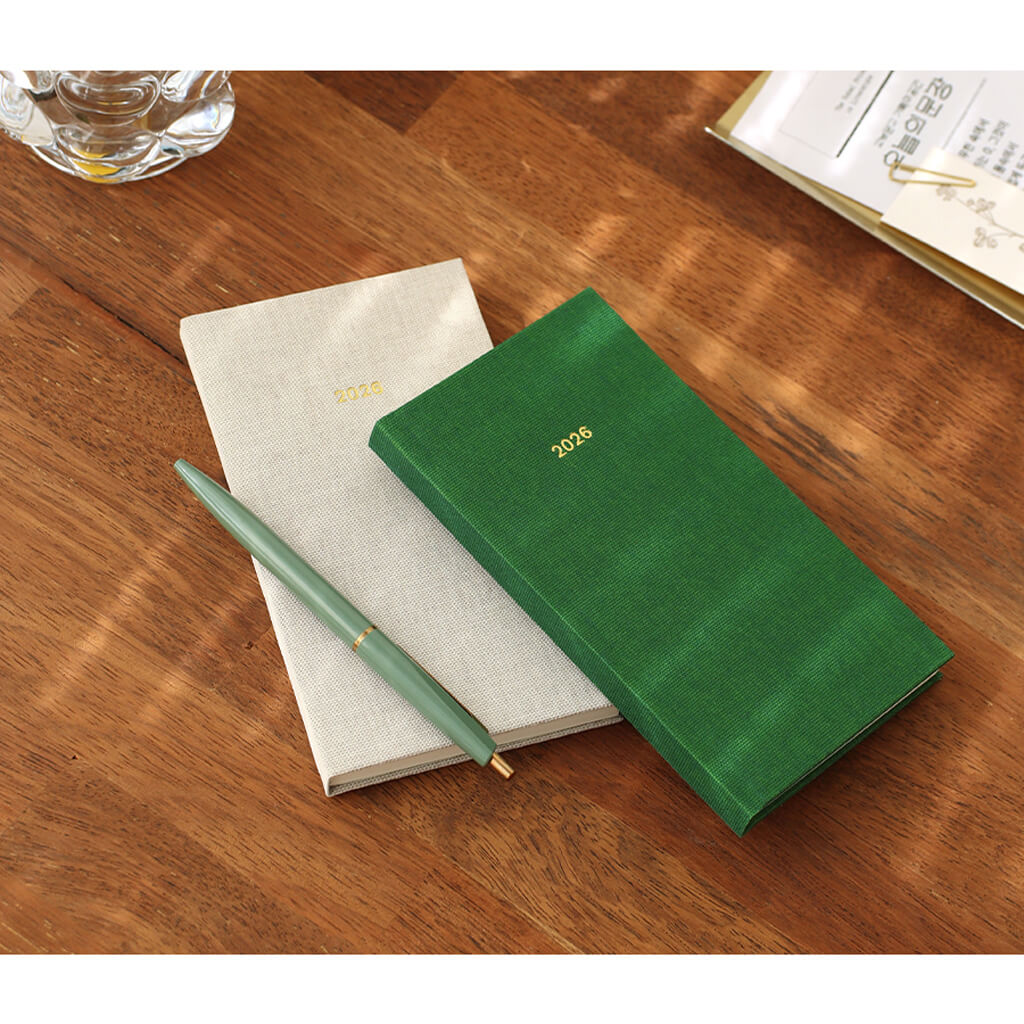 Green weekly planner with a minimalist design and pen on a wooden surface