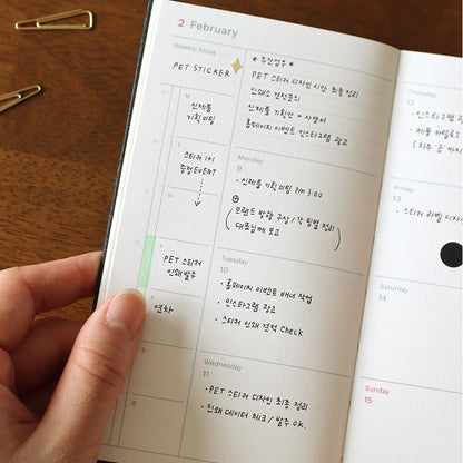 Hand holding a dated weekly planner with handwritten notes on a wooden surface