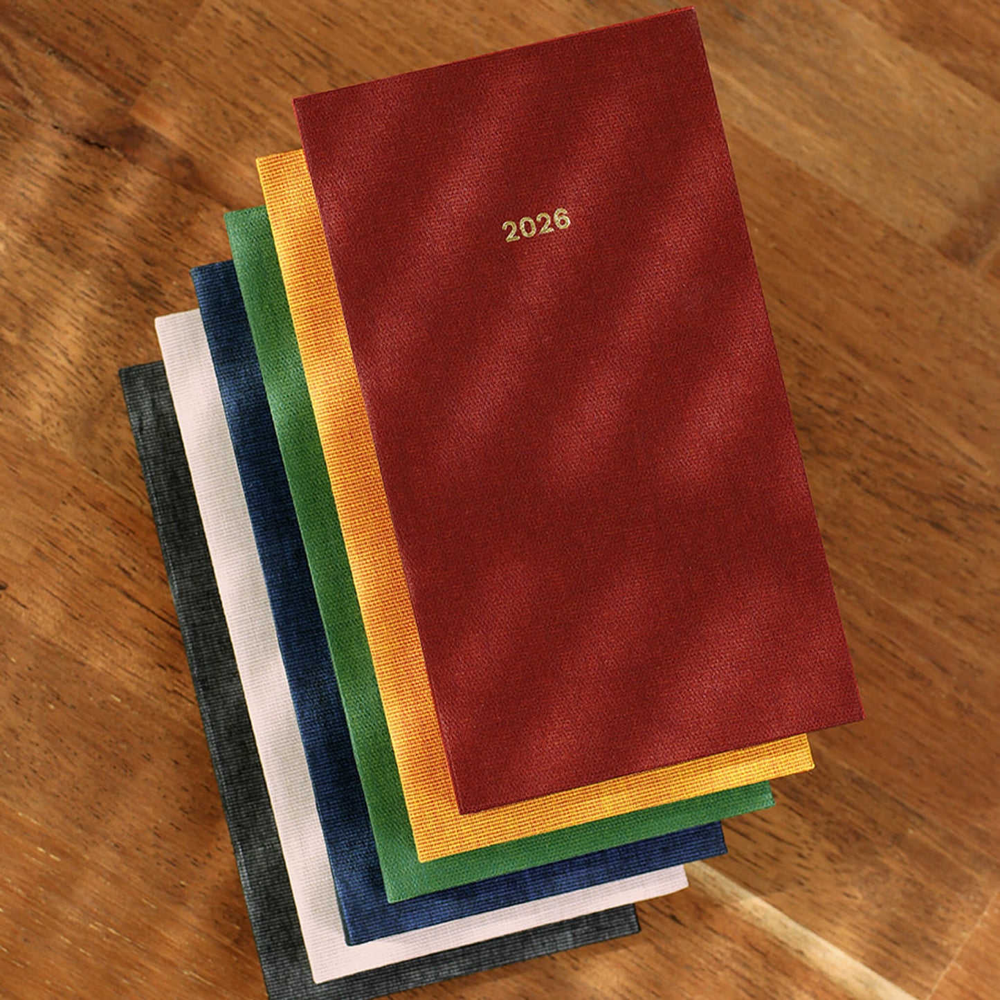 Stack of colorful cloth-cover diaries with '2026' on a wooden surface