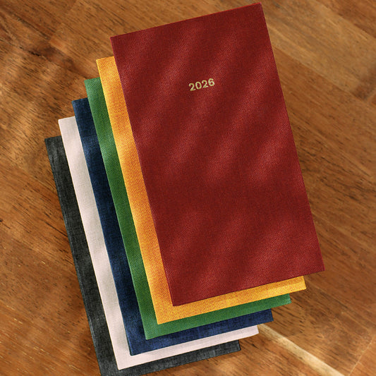 Stack of colorful cloth-cover diaries with '2026' on a wooden surface